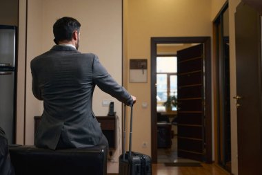 Kanepenin arkasında takım elbiseli bir otel müşterisi oturuyor, cep telefonuyla iletişim kuruyor.