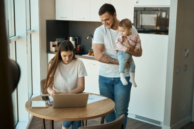 Modern kadınlar mutfakta, kucağında bir çocukla kocasının yanında uzaktan çalışırlar.