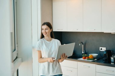 Gülümseyen uzun saçlı esmer ayakta durup geniş bir pencerenin önünde dizüstü bilgisayarla uzaktan çalıştığını düşünüyordu.