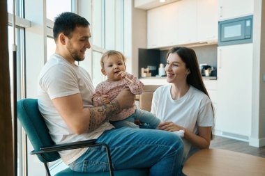 Genç aile mutlu bir şekilde mutfakta vakit geçiriyor, küçük kızın elinde bir kalem var.