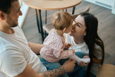 Ebeveynler mutlu bir şekilde küçük kızlarıyla mutfakta vakit geçiriyorlar. Bebeğin elinde bir kalem var.