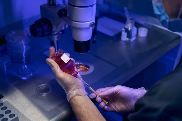科研人员用注射器从小瓶中取出液体样本 在显微镜下进行研究 — 图库照片