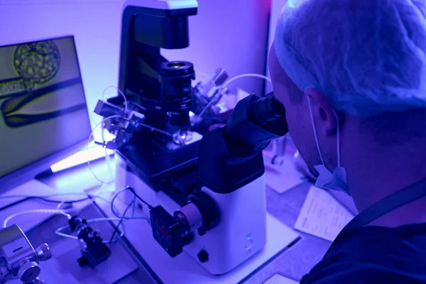 生殖学实验室工作人员在显微镜下检查眼睛镜片 并与微操作人员一起工作 向卵母细胞注射药物 — 图库照片