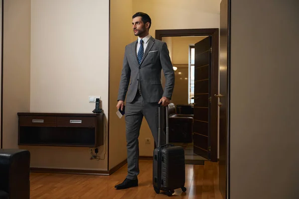 带着旅行箱的男人站在酒店房间里 穿着西装 — 图库照片