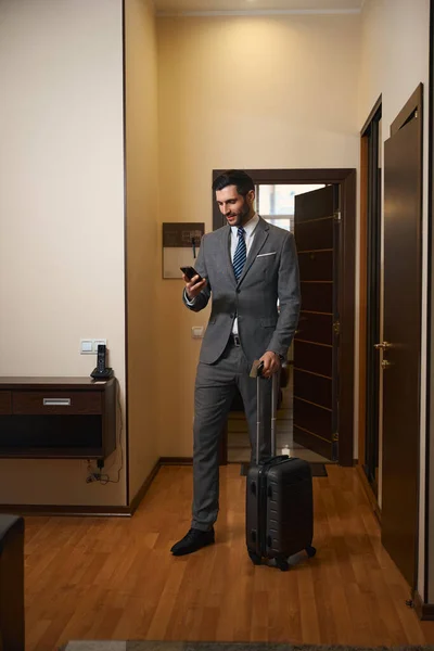 携帯電話で話しているビジネスマンの笑顔 男は旅行スーツケースを持っている — ストック写真