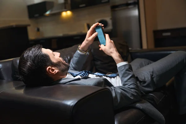 旅馆的客人在房间里的皮革沙发上休息 他在用手机 — 图库照片