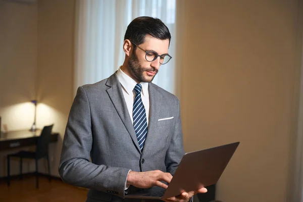 戴着眼镜的优雅男性站在宾馆房间里 手里拿着笔记本电脑 男人穿着时髦的西服 — 图库照片