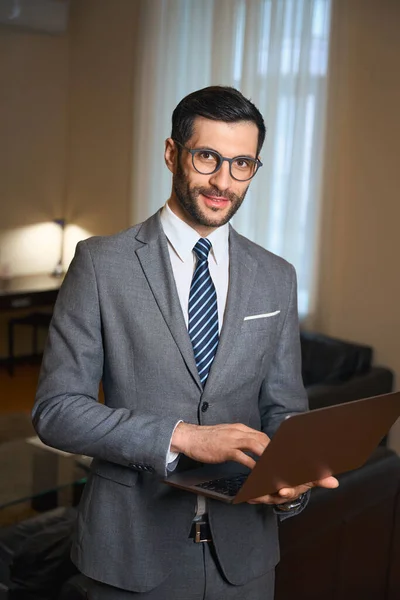 一个戴着眼镜的漂亮的黑发女人站在酒店房间里 手里拿着笔记本电脑 男人穿着西服 — 图库照片
