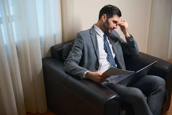 Zmęczony Biznesmen Siedzi Skórzanym Krześle Dokumenty Robocze Laptopa — Zdjęcie stockowe