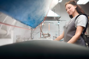 Kuru temizleme işinde usta bir kadın. Kırışıklıkları gideriyor. Buhar ütüsüyle giysileri ütülüyor.