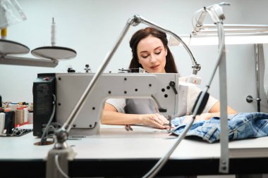 Çamaşır işçisi kadın işçiler dikiş makinesindeki kıyafetleri onarıyor, pantolon paçasını düzeltiyor fermuar ve düğmeleri tamir ediyorlar.