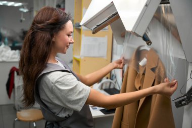 Kadın çamaşırhane işçisi temiz ve kuru paltoyu selofan çantaya koyup, giysiyi paket yaptırmaya hazırlıyor.