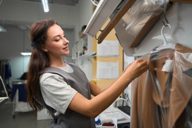 Kuru temizlemeci kadın temiz, teslimata hazır, profesyonel giysi bakımı için plastik torbaya etiket yapıştırıyor.