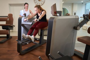 Kliniğin müşterisi modern bir fitness makinesinde çalışıyor. Yanında da antrenör-danışman var.