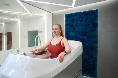 Kliniğin müşterisi su simülatörünün üzerinde duruyor. Kapalı alanda dengelenmiş yosunlardan yapılmış dekoratif bir panel var.