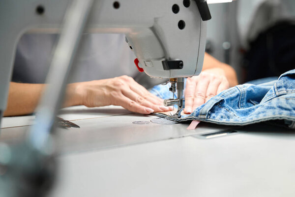 Женский портной работает на швейной машине, добавляя ярлыки к одежде после химчистки, залатав отверстия, качественное обслуживание