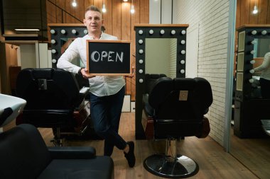 Aynaların önündeki berber dükkanında açık tabelalı berber ve rahat kuaför koltukları.