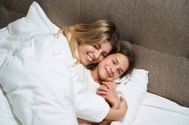 Mutlu anne yatağında dinleniyor ve otel odasında ona sarılıyor.