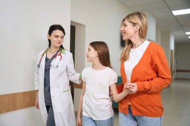 Gülümseyen kadın pediatrist kompleks sağlık kontrolünden önce küçük kızı sakinleştiriyor ve destekliyor.