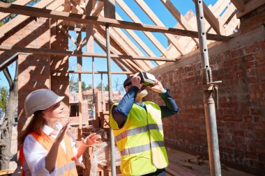 Sanal gerçeklik gözlüğü takan erkek müşteri bina üstüne ev görmek için onunla tasarım ve kalite hakkında konuşan kadın mimar.