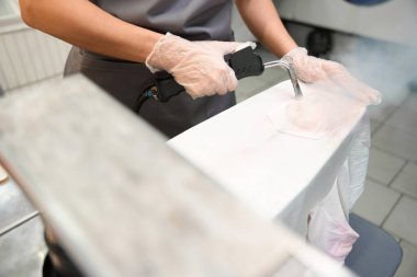 Çamaşır istasyonu çalışanı ön tedavi yapıyor, buhar tabancası kullanarak lekeleri tanımlıyor ve çıkarıyor.