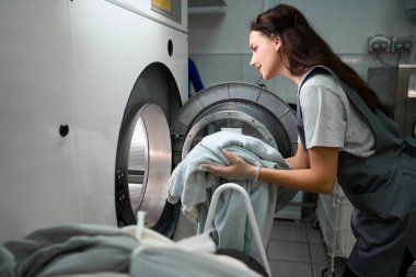 Kadın kuru temizlemeci davul makinesini leke ve lekelerle dolduruyor, profesyonel çamaşır servisi.