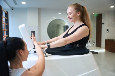 Klinik çalışanları spor giyinen kadınlara spor salonunda müşterilerine yardım ediyor.