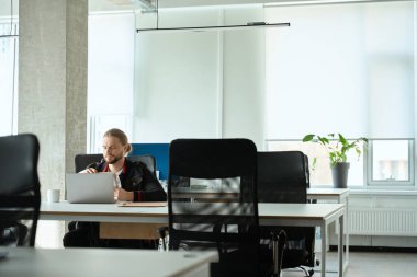 Genç adam parlak bir odada dizüstü bilgisayarda çalışıyor. Odanın içinde minimalist bir iç mekan var.