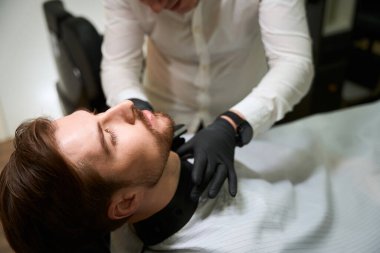 Erkek, müşterinin boynundaki kılları özel bir budayıcıyla tıraş eder. Adam profesyonel yüz bakımını tercih eder.