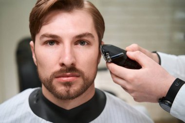 İş yerindeki kuaför erkek bir müşteriyle çalışıyor. Odanın modern bir iç mekanı ve mükemmel ışıklandırması var.