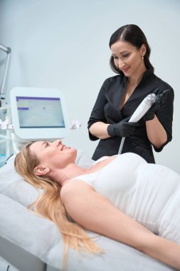 Müşteri ve kozmetolog RF kaldırma prosedüründen önce iletişim kurar, uzman modern ekipman kullanır.