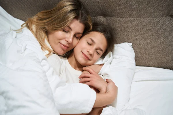 女人躺在靠近女儿的床上 在旅馆房间里拥抱她 — 图库照片