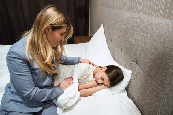 穿着西装的女人坐在床上 看着宾馆里休息的女儿 — 图库照片