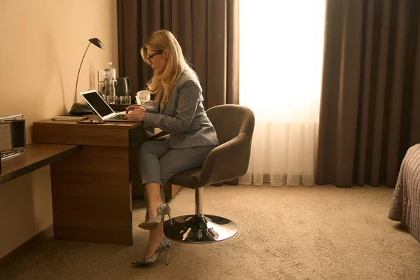 Elbiseli Bir Kadın Otel Odasında Oturmuş Dizüstü Bilgisayarla Çalışıyor — Stok fotoğraf