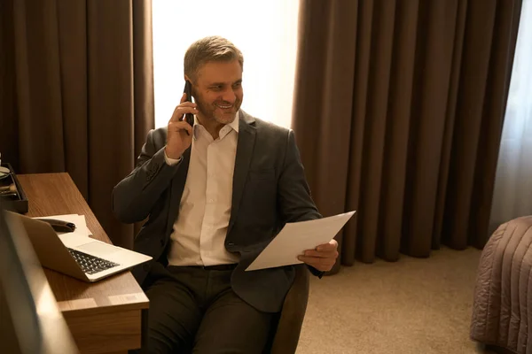 大人の男性ビジネススーツの椅子に座って電話をかけモーテルの書類を見て — ストック写真