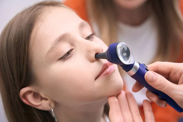 近くの女性の喉頭科医は女の子の鼻をチェックし ポリープを調べ 治療を処方するための問題を診断する — ストック写真