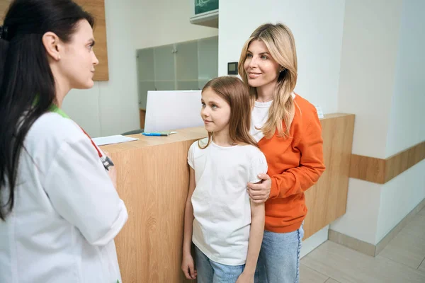 小さな患者と彼女の母親に挨拶し 医師の任命 健康診断の準備をする民間のクリニックの管理者 — ストック写真