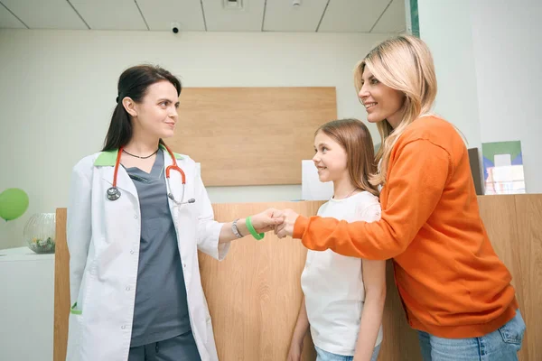 优雅的母亲与小女儿的儿科医生握手 带着孩子去看医生 抱怨自己的健康状况 — 图库照片