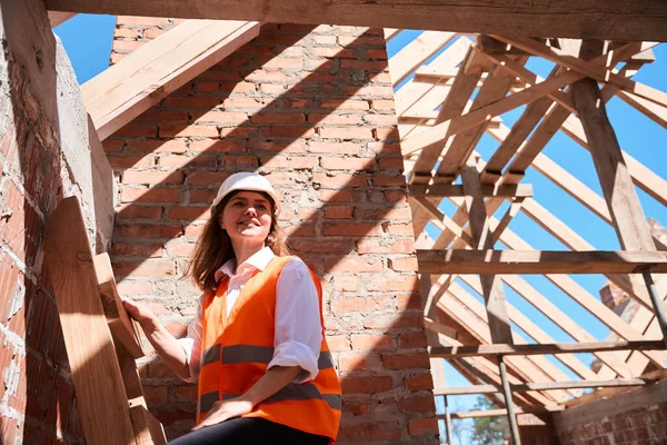 プロのプロジェクトの図面に満足し 屋根の梁や床を構築するために木製のはしごを登るのは難しいで正の女性建築家 — ストック写真