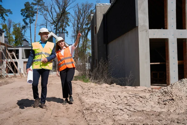 建設現場を歩いて設計図を持つ女性の建物のエンジニアとフォアマン 民間住宅都市の建物の進捗状況を確認します — ストック写真