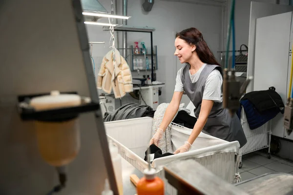 洗濯機の洗浄前に汚れや涙の有無を確認し 衣類を選別する笑顔の女性ドライクリーニングオペレーター — ストック写真