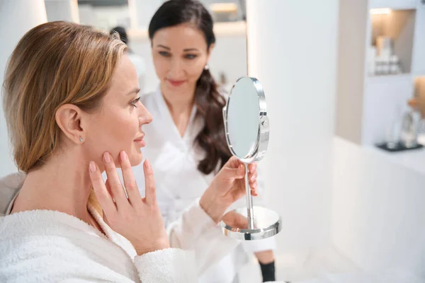 美しい女性は鏡の中を見ます美容師と相談して制服の専門家 — ストック写真