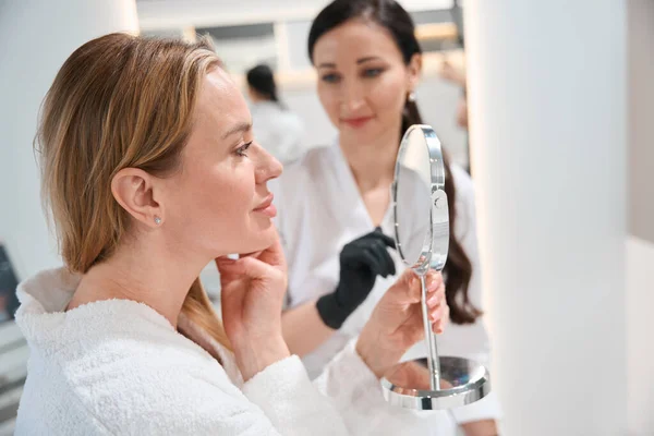 Mujer Encantadora Mira Espejo Una Consulta Con Médico Esteticista Especialista — Foto de Stock