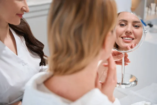 笑顔の女性ブロンドは美容師と相談して鏡を見て 彼女は鏡の中の反射に満足しています — ストック写真