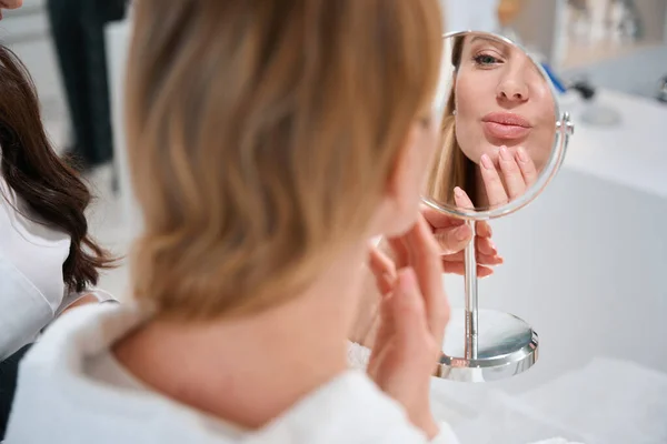 Szőke Tükörbe Nézi Arcát Egy Kozmetikussal Konzultálva Elégedett Tükörképpel — Stock Fotó