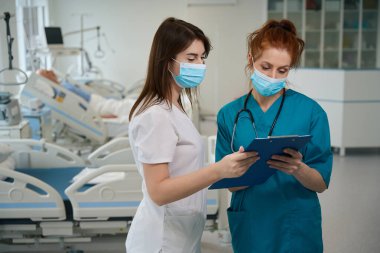 Kağıt kağıtlarla panoya bakan ve hastanede hasta teşhisini tartışan konsantre tıp uzmanları.