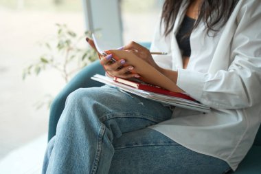 Afro-Amerikalı bir kadının, kanepede otururken kalemle not aldığı görüntüler.