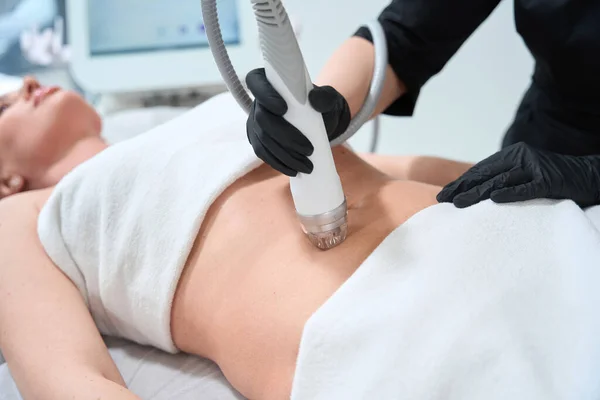 年轻女人躺在美容沙发上 美容师为她的腹部做射频提升手术 — 图库照片