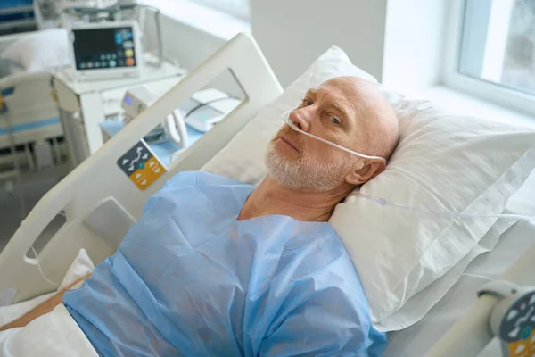 病院の集中治療室でベッドの上に横になっている間 男性患者は鼻管を通して補足酸素を得る — ストック写真