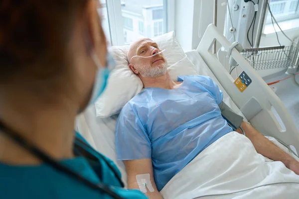 病院のベッドに横になっている間に診療室で酸素を得る男性患者の健康について学ぶ女性医学の作物の写真 — ストック写真